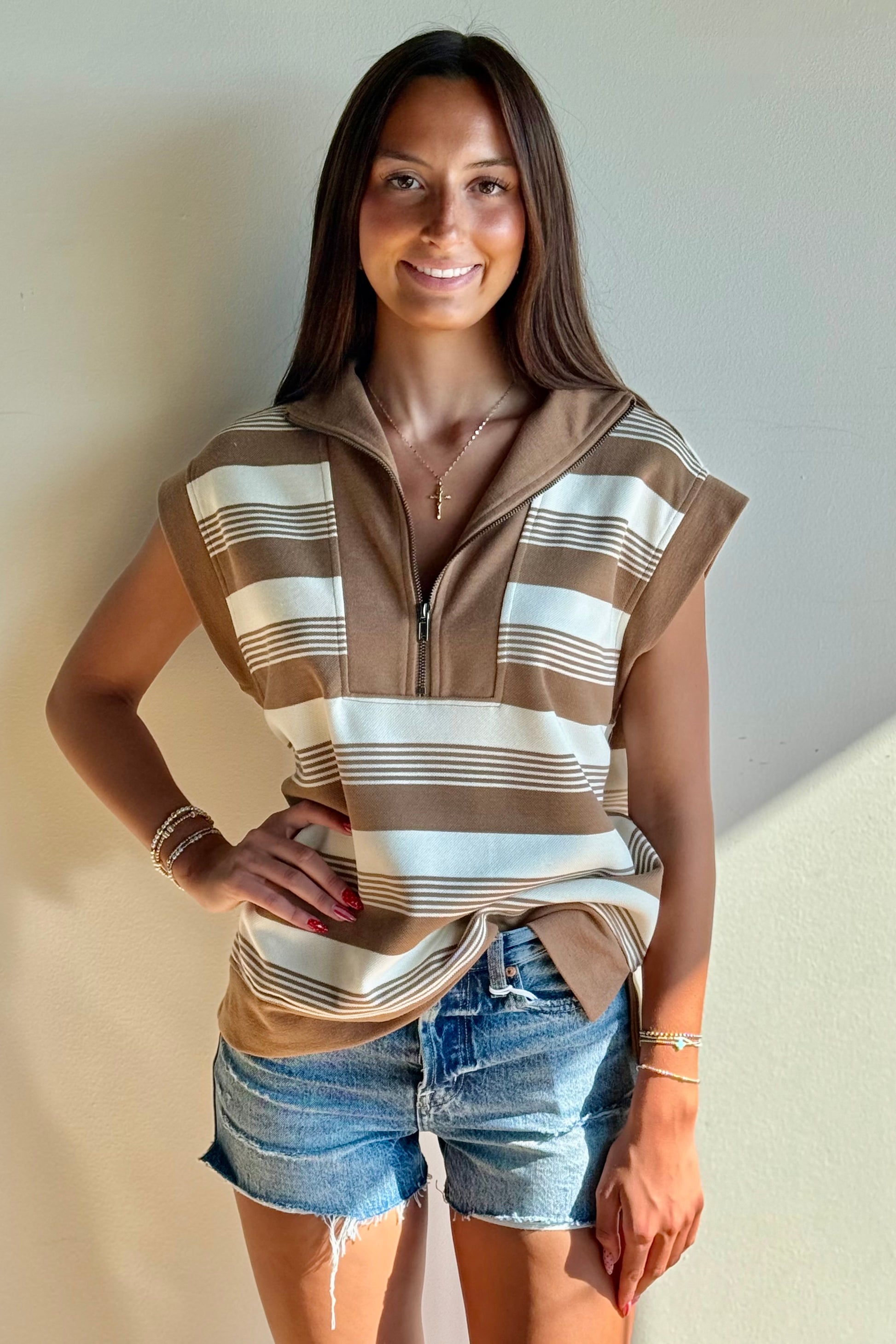 Woman wearing a striped shirt and denim shorts against a plain background